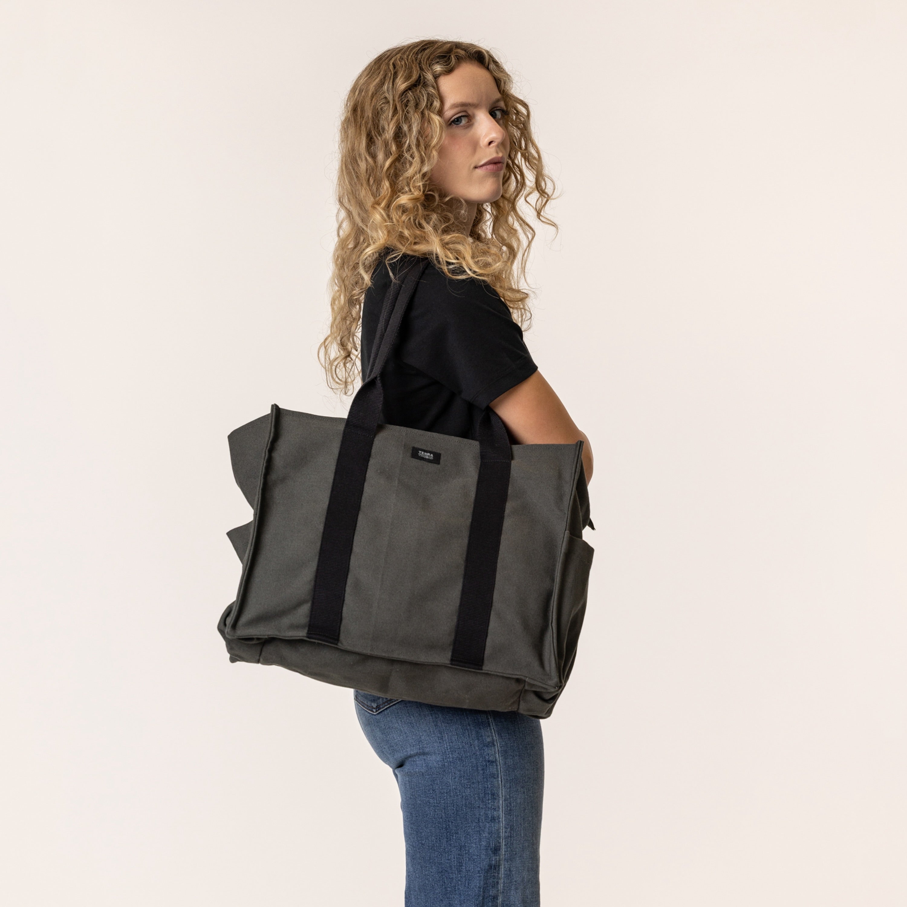 Woman holding a large charcoal grey sustainable handbag with black straps