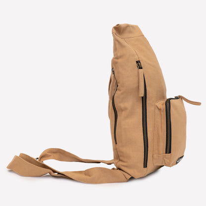A khaki color canvas sling bag with multiple black zippers